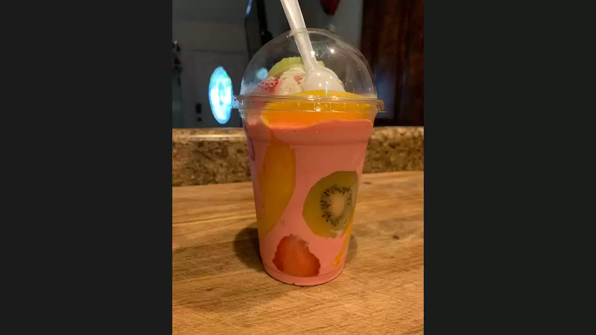 A fruity yogurt shake with kiwi, strawberry, and orange pieces in a clear cup with a straw.