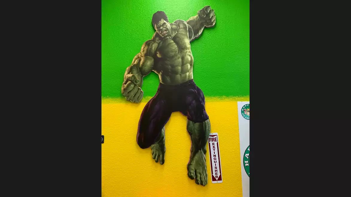 Image of a large, green, muscular comic character on a yellow-green wall.