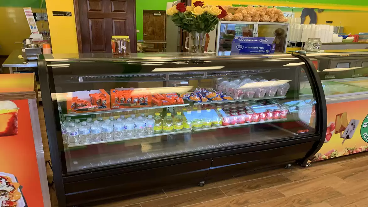 Refrigerated display case with various drinks and snacks in a store. Flowers and rolls are visible in the background.