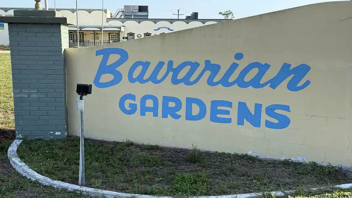 A beige wall with the text 'Bavarian Gardens' in blue letters on a sunny day.