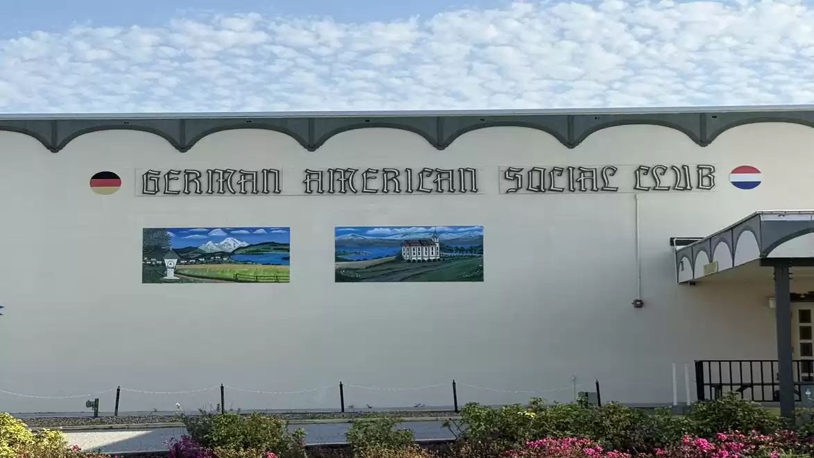 Building with the sign 'German American Social Club', wall paintings, and flower garden.