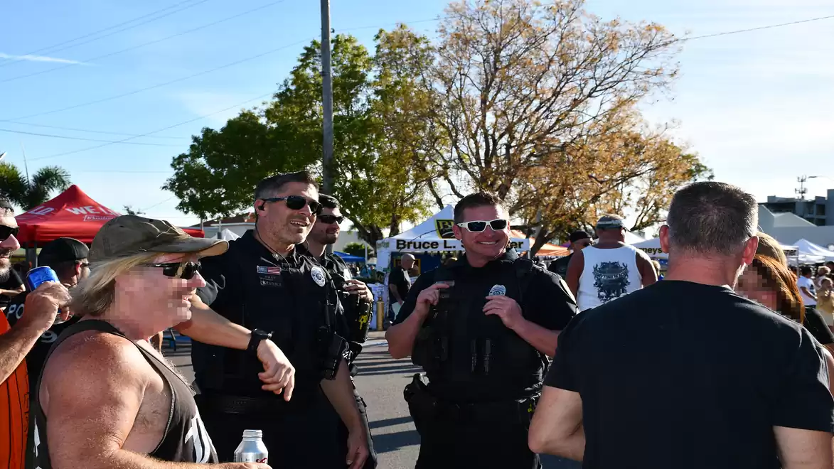 Group of people at an outdoor event with police officers and attendees under a blue sky.