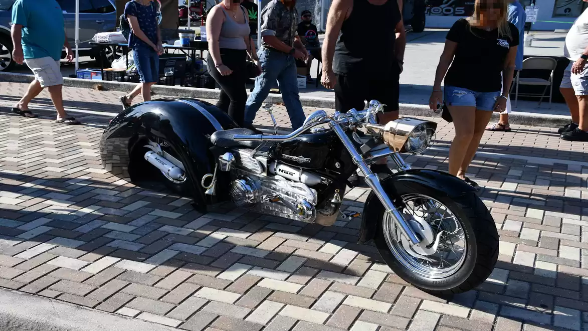 Black custom motorcycle on a cobblestone street with people in the background.