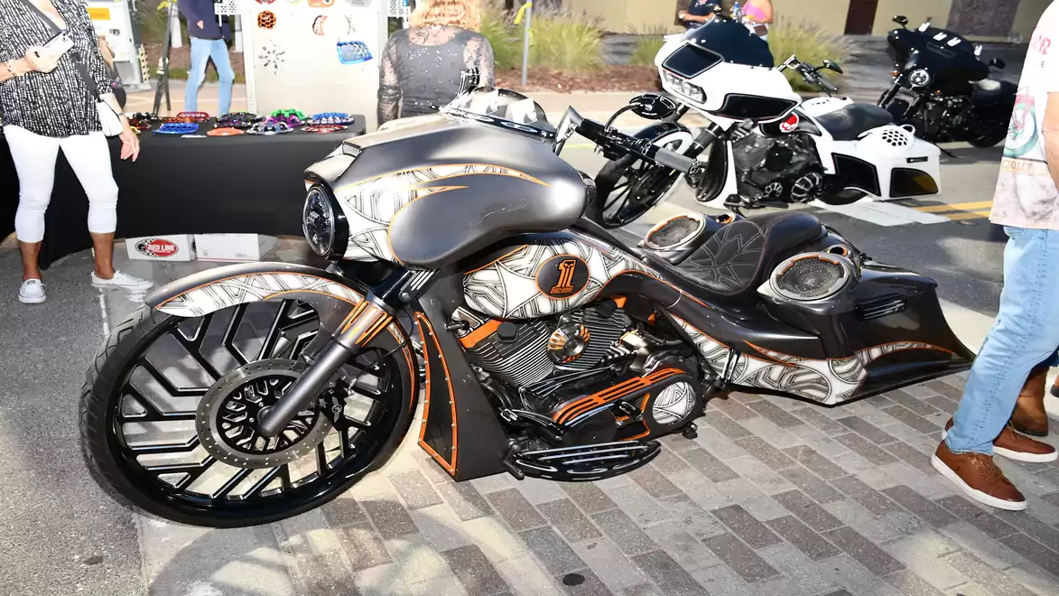 A heavily customized motorcycle with a striking design at an exhibition, surrounded by people and other vehicles.