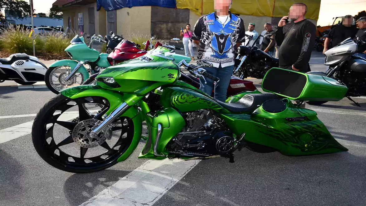 A green custom bike with a striking design is parked on a lot, surrounded by several people and other motorcycles.