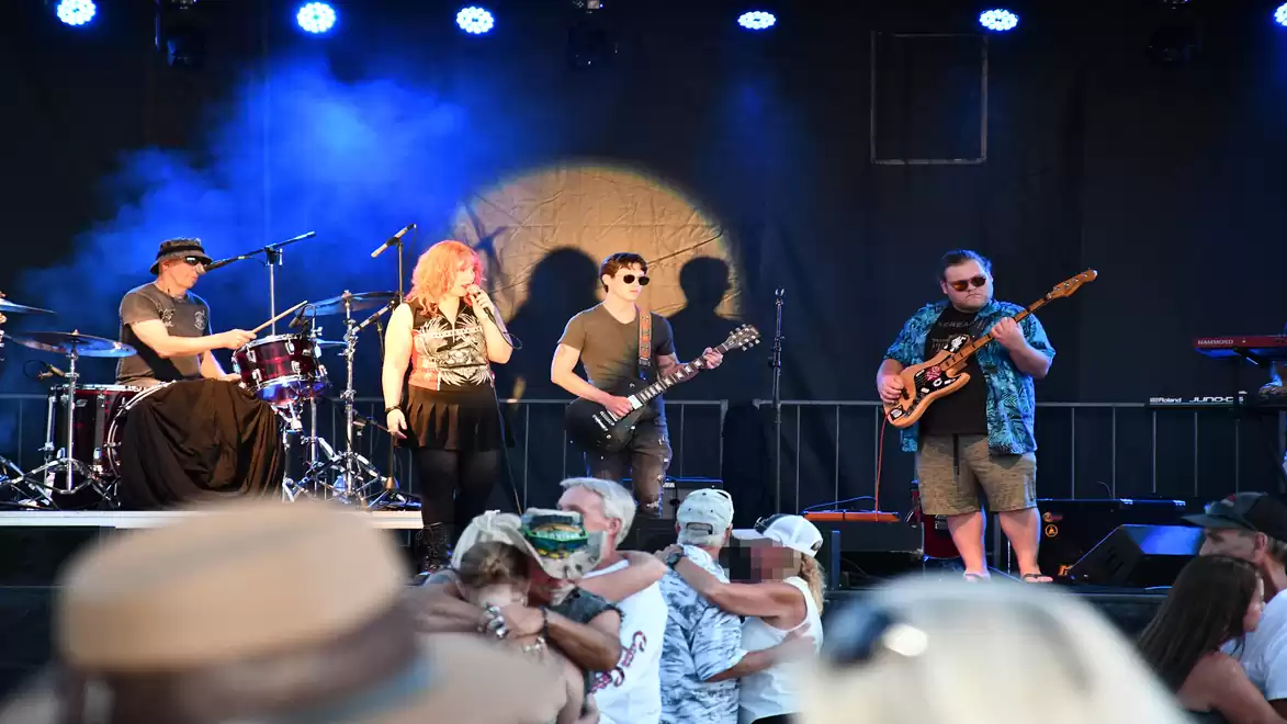 Band performing live on stage with blue lighting and audience in the foreground.