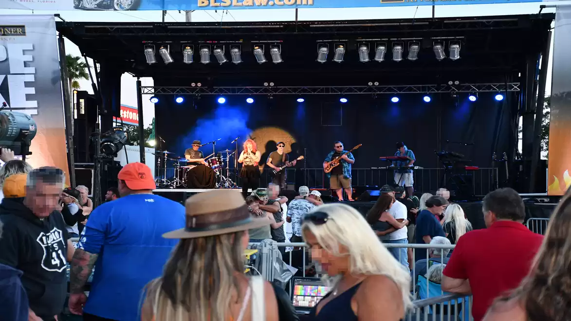 A live band performs on a stage at an open-air concert, surrounded by an enthusiastic audience.