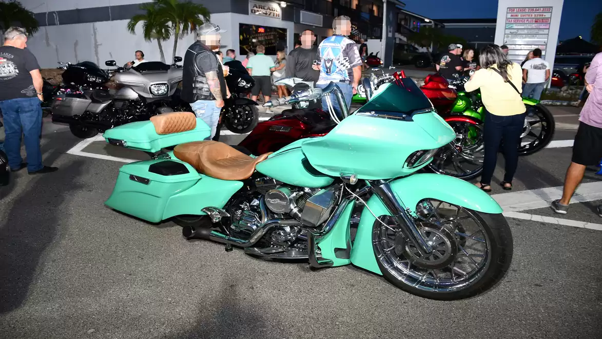 A mint green motorcycle with brown leather details is parked in a lot. Several people are standing nearby looking at the displayed motorcycles.
