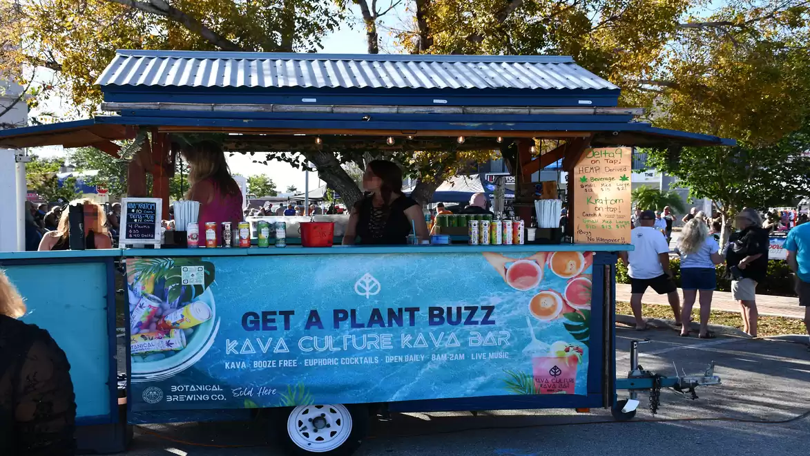 A mobile Kava bar stand with the sign 'Get a Plant Buzz' and people preparing drinks.