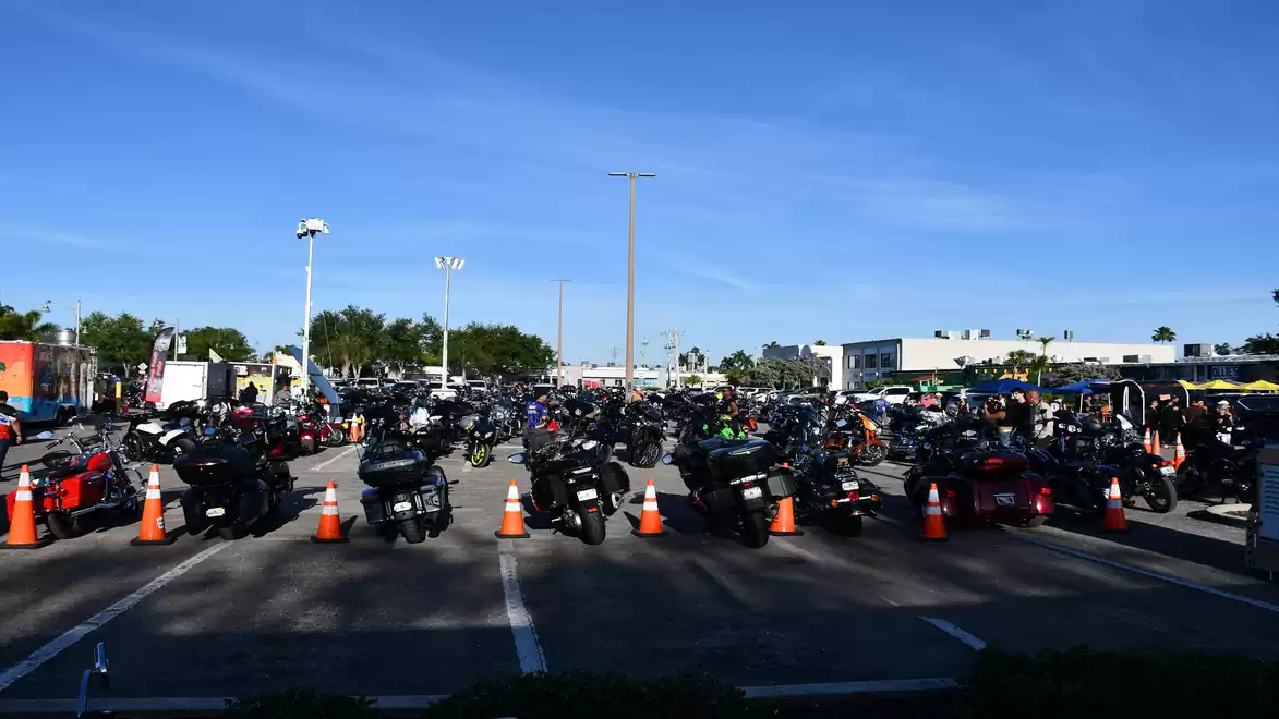 A parking lot full of motorcycles under sunny weather in front of a shopping center.