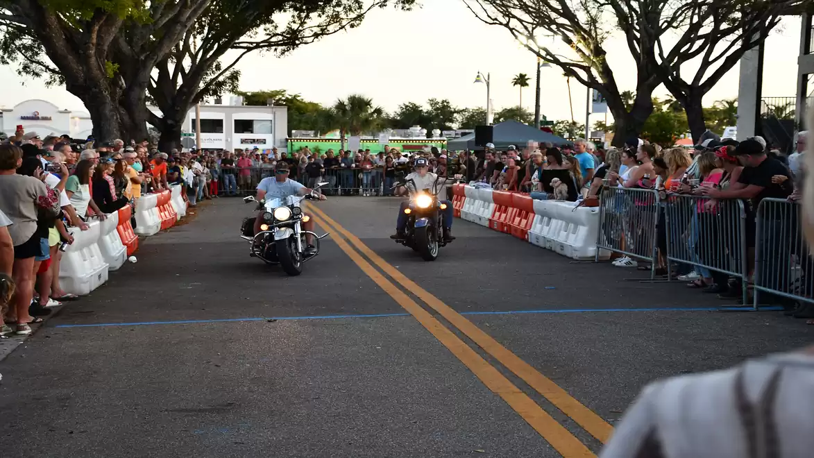 Two motorcyclists riding on a street race track, lined with spectators behind barriers.