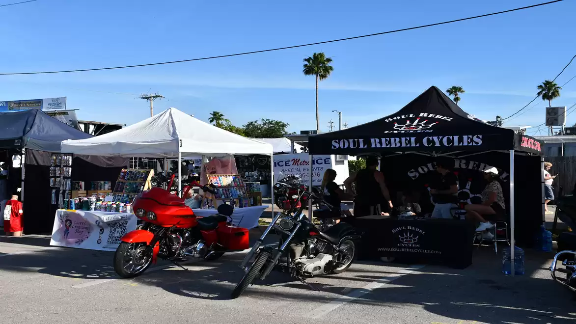 An outdoor motorcycle market with various booths and displayed motorcycles under a blue sky.