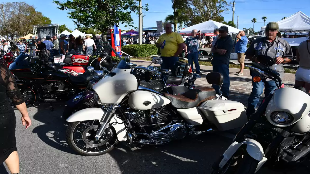 People gather at an outdoor motorcycle show with various bikes and tents in the background.