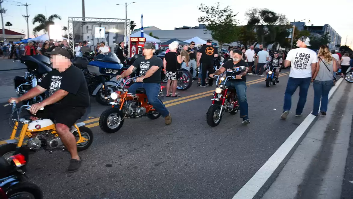Street gathering with people riding small motorcycles and gathering in the background.