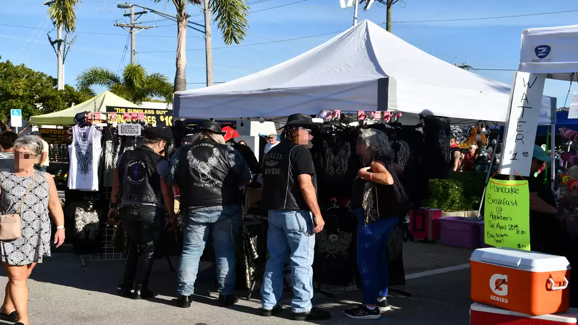 People at a street market with a white tent and stalls selling motorcycle apparel.