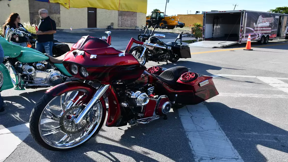 Stylish red motorcycle with chrome wheels parked in a parking lot next to other bikes on a sunny day.