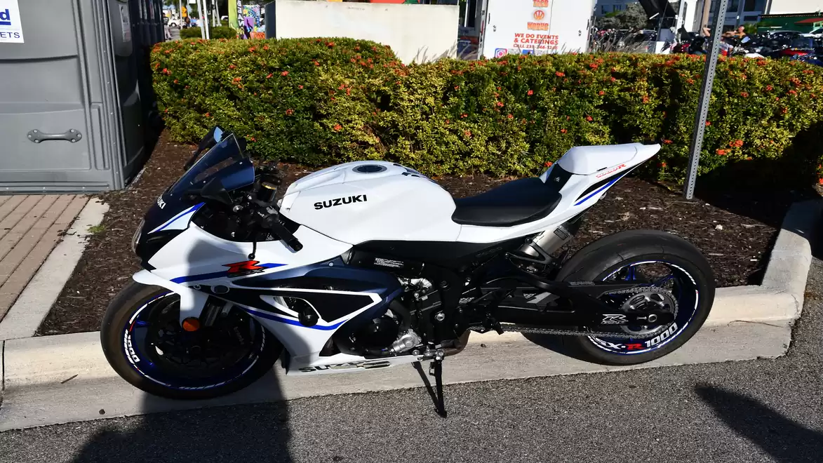 White Suzuki GSX-R on a parking lot with green bushes in the background.
