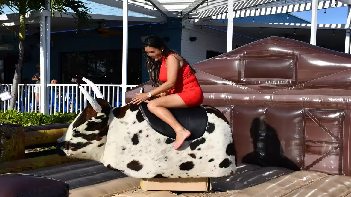 A woman in a red dress riding a mechanical bull in an outdoor setting.