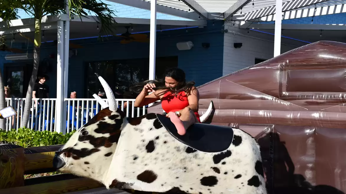 A woman in a red top riding a mechanical bull in an outdoor setting.