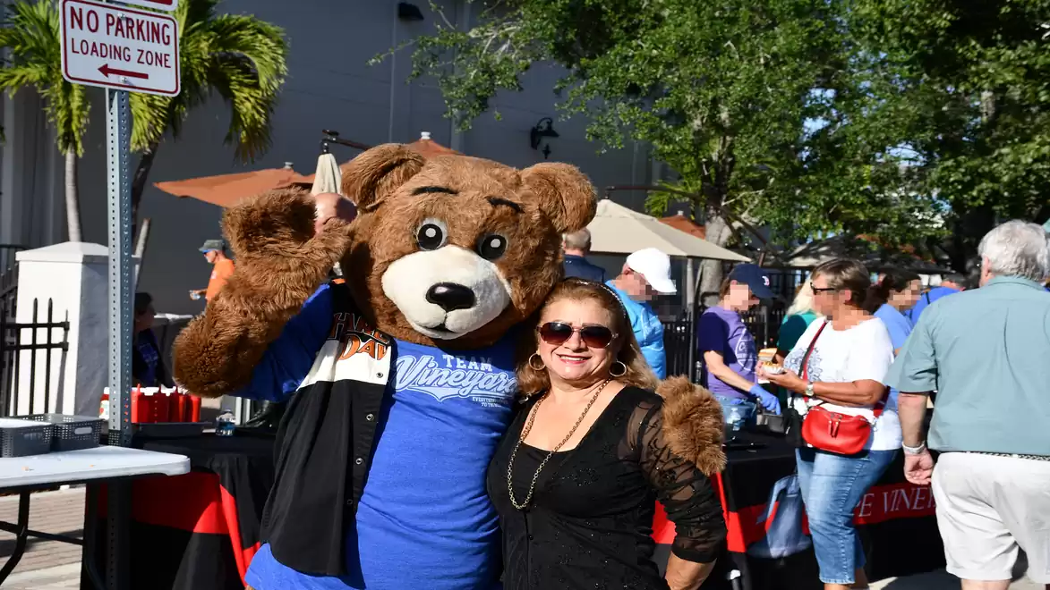 A smiling woman poses next to a person in a bear costume at an outdoor event.