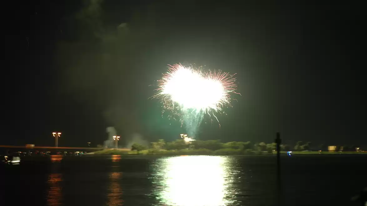 A fireworks display lights up the night sky over a body of water, reflecting the light.