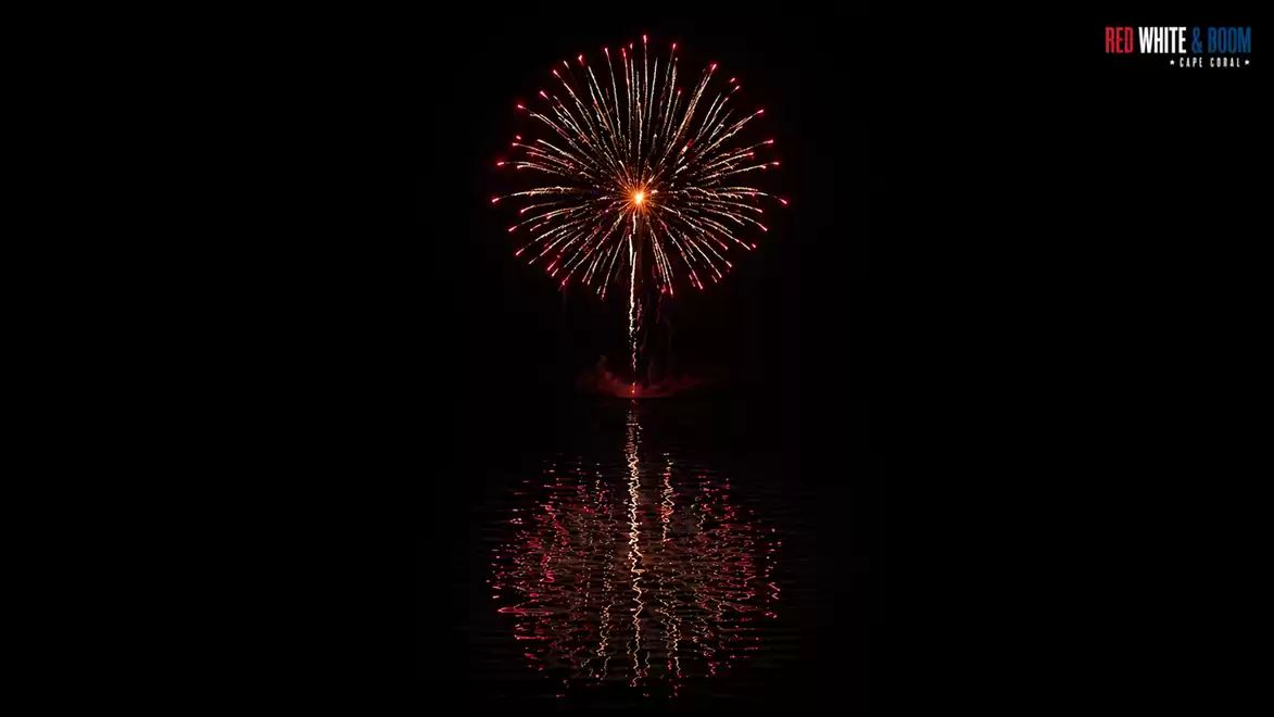 A fireworks display with red and orange sparks reflecting on the water against a dark night sky.