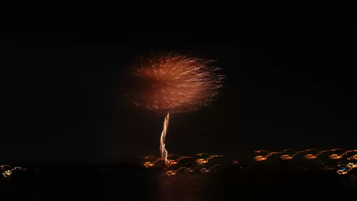 A single firework shines brightly in the night sky over a cityscape.