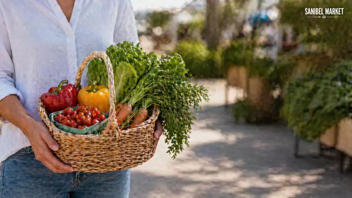 A person holds a basket of fresh vegetables including peppers, tomatoes, and carrots at an outdoor market.