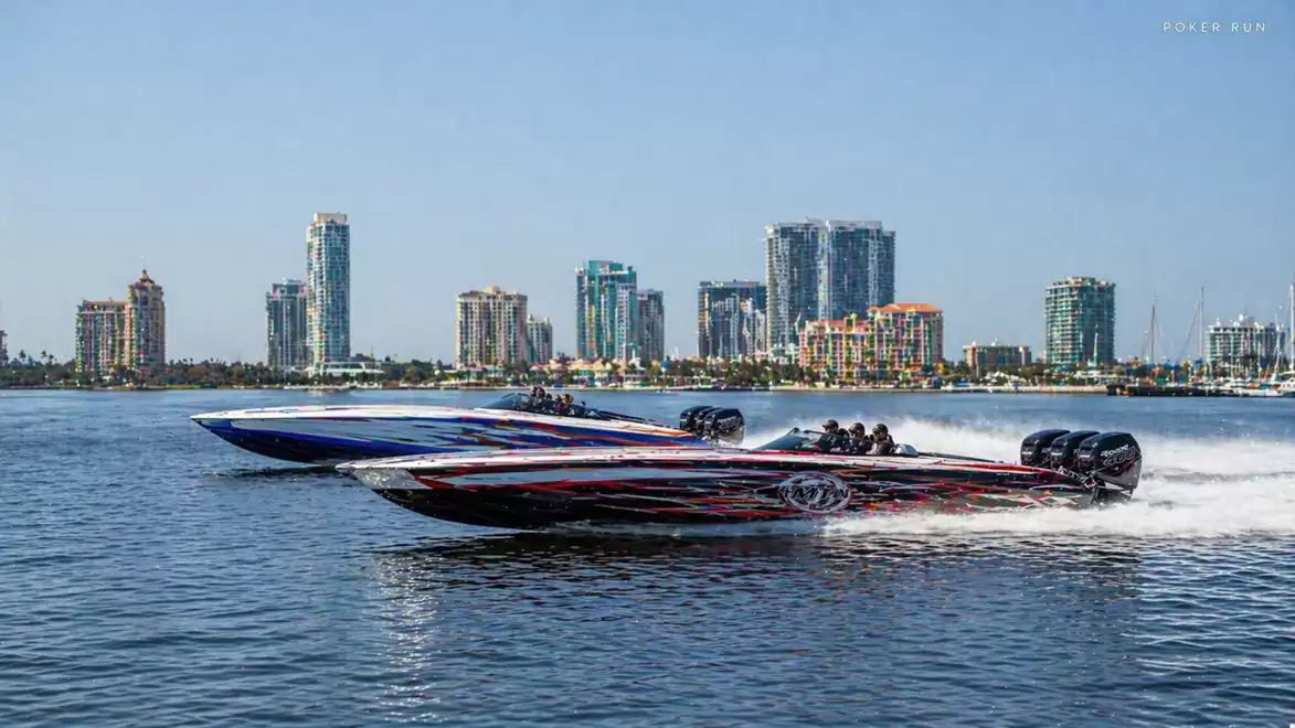 Two racing boats side by side on the water with a skyline of skyscrapers in the background.