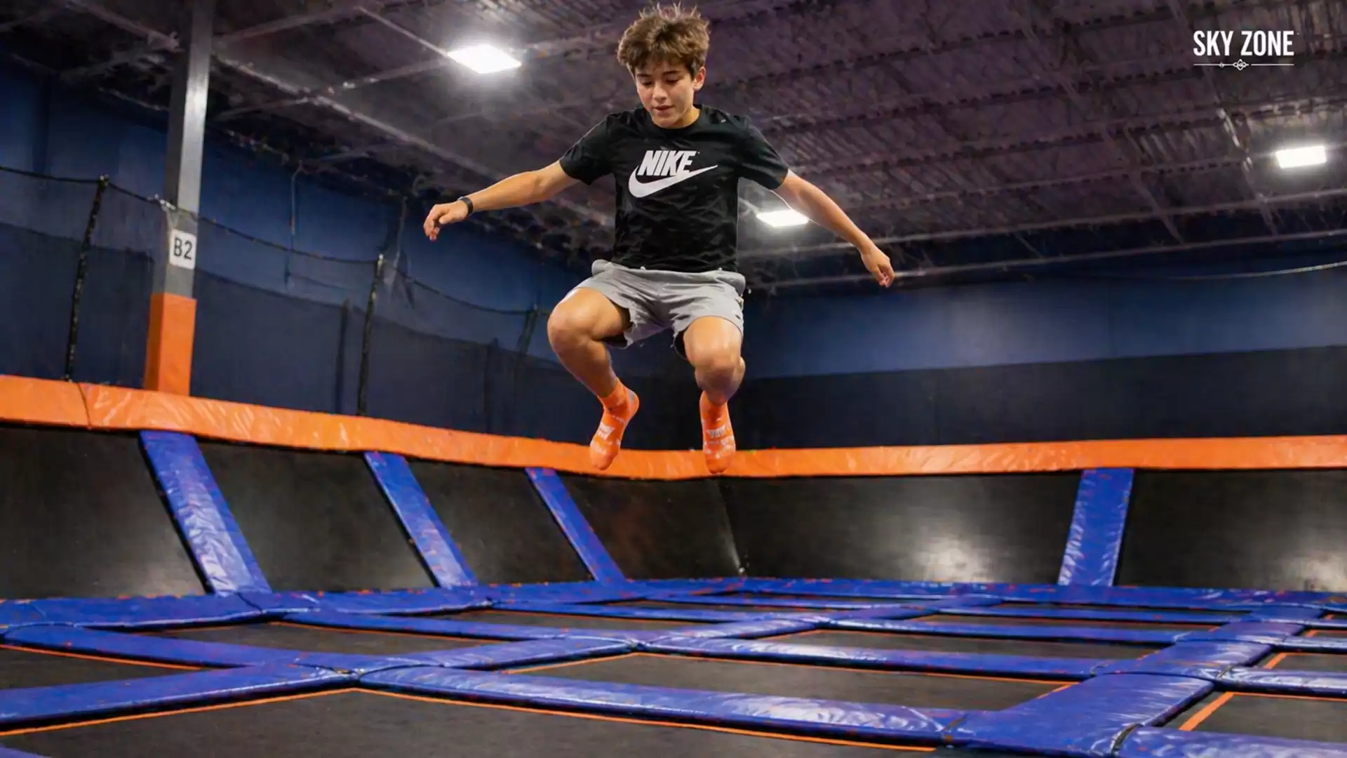 A boy jumping on a trampoline in an indoor facility with blue and orange elements.