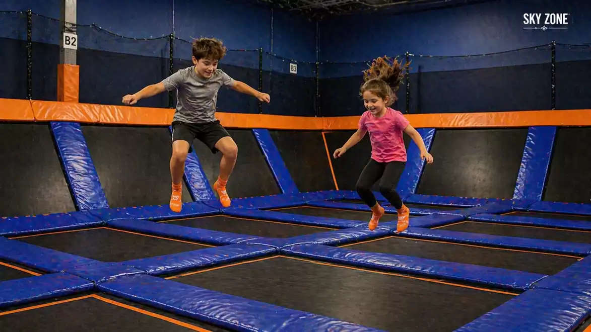 Two children jumping on trampolines in a trampoline park with orange and blue mats at Sky Zone.