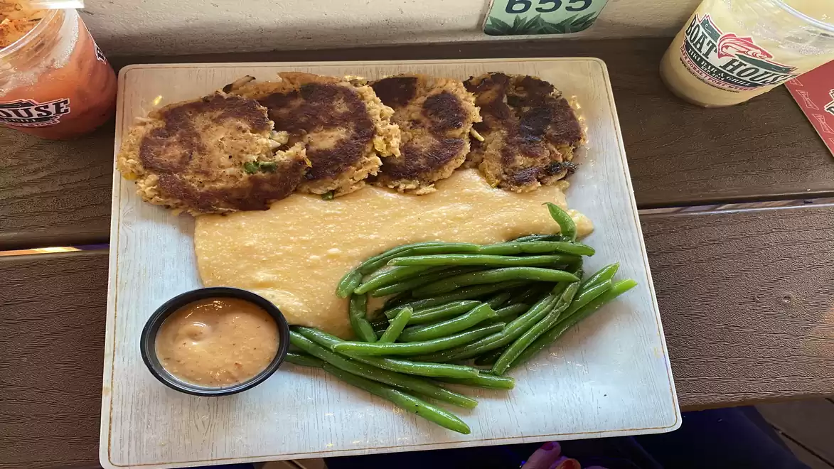 A square plate with four patties, green beans, mashed potatoes, and a small cup of dipping sauce.