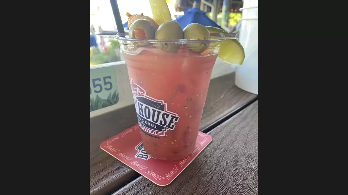 A cup with a pink drink, garnished with green vegetables and lime slices, placed on a table.