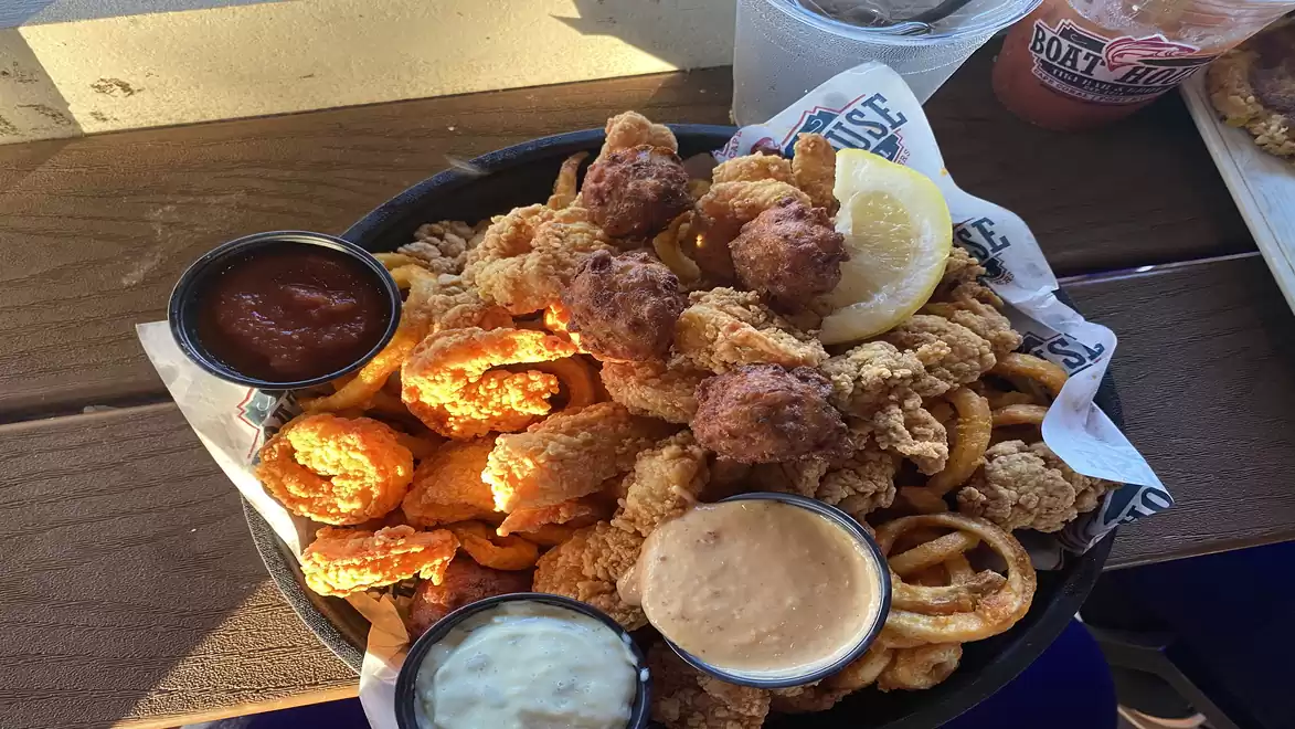 A plate of fried fish and seafood served with various sauces, lemon, and sides on a wooden table.