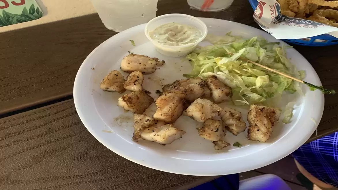 A plate with grilled chicken and salad, served with a small bowl of dip sauce, on a wooden table.