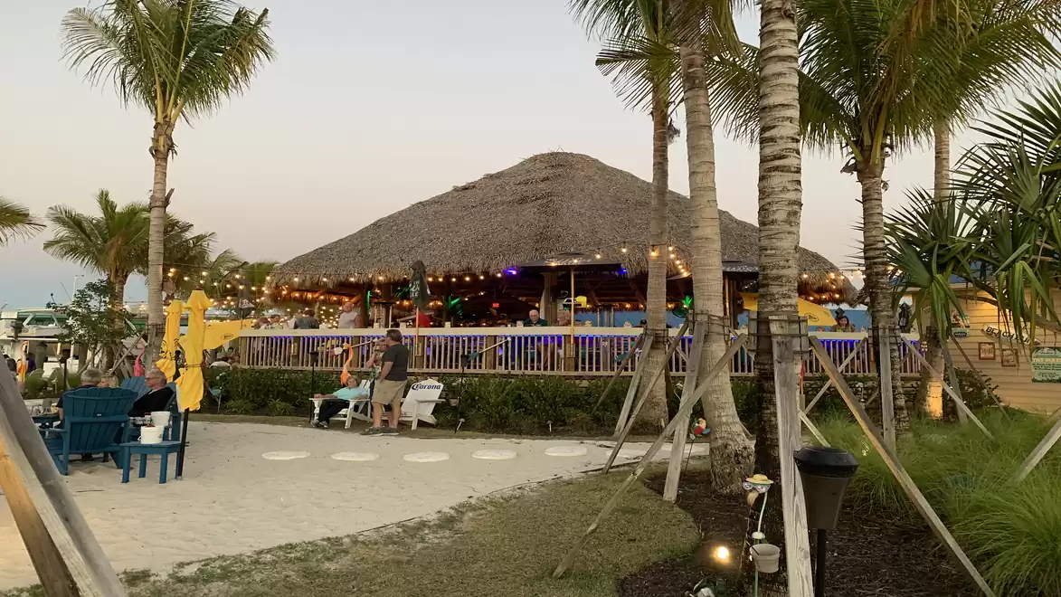 Palm-lined beach restaurant with a thatched roof at sunset, people relaxing in the area.