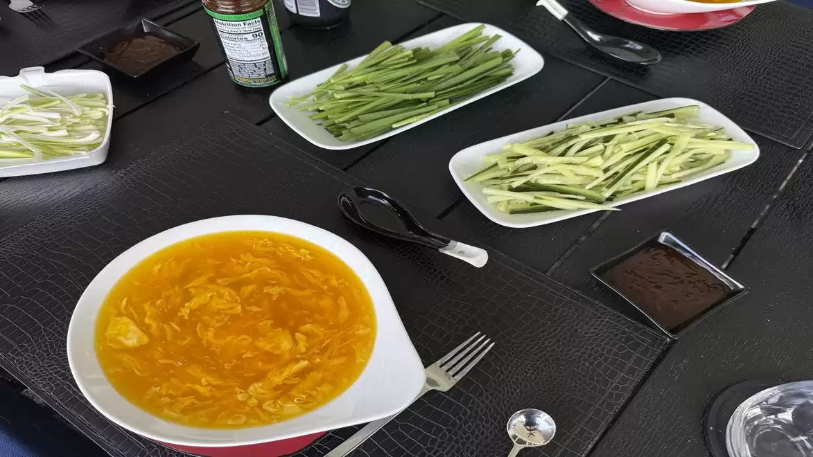 A dining table with bowls of Spinach Egg Drop soup and sliced vegetables on black placemats.