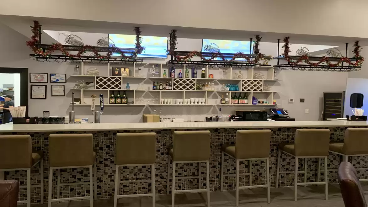A modern bar with beige upholstered stools, white shelves with wine bottles, and an intricate model of a miniature train above the counter.