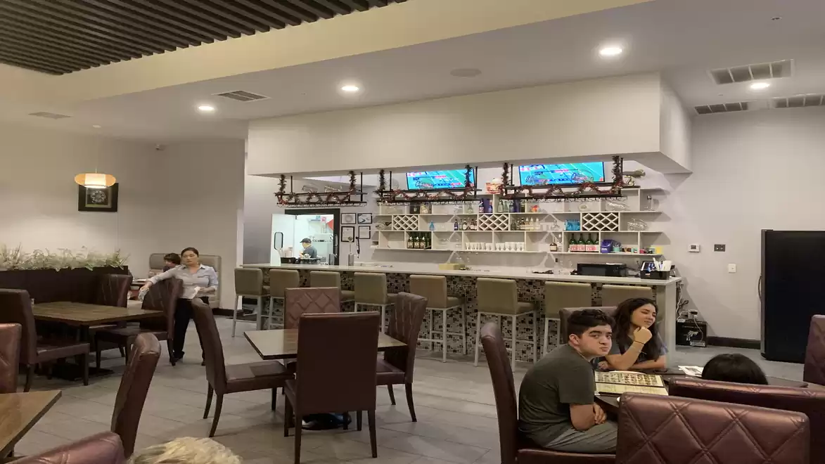 A modern restaurant with a bar in the background. People are sitting at tables and chatting.