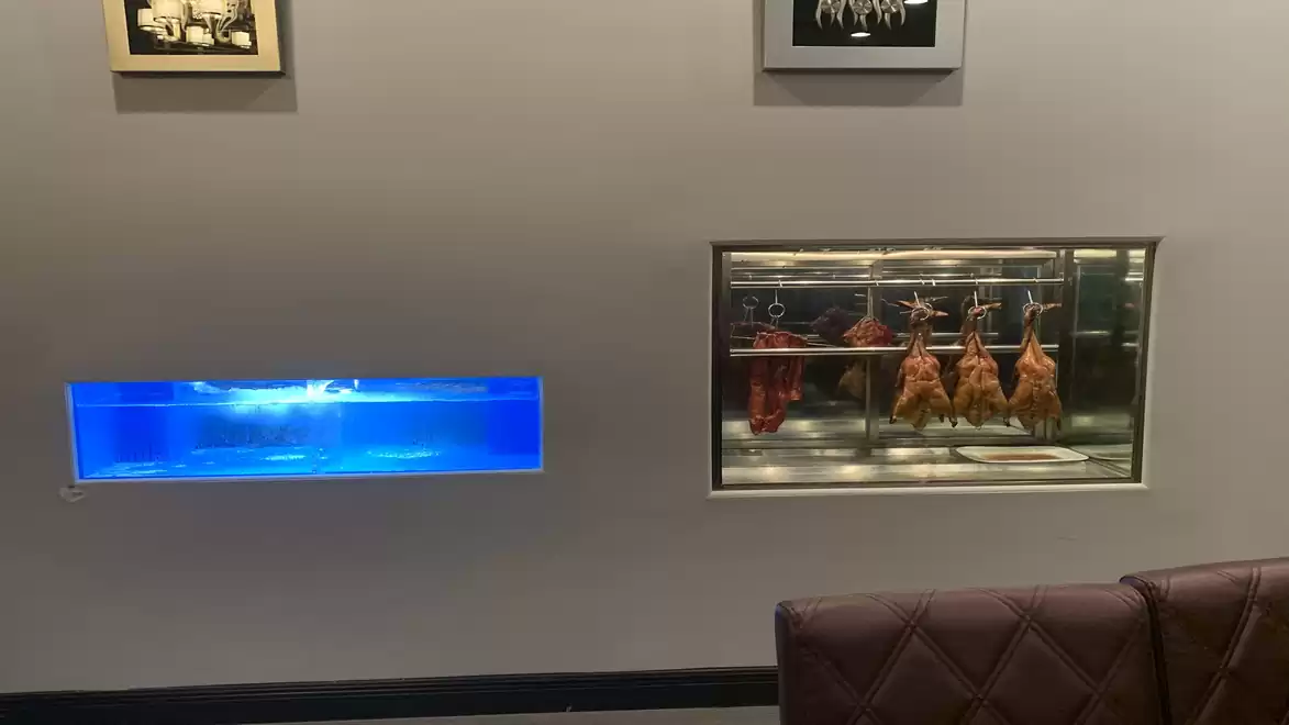 Interior of a restaurant featuring an aquarium and a glass display case with roasted ducks.