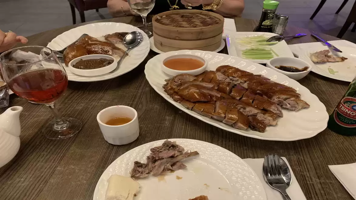 A set table with duck dishes, sauces, a teapot, and drinks in a restaurant.