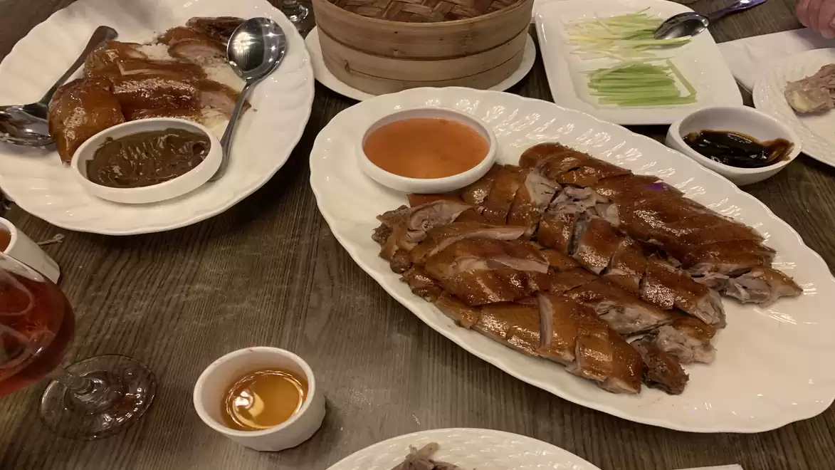 A table with traditional Chinese food. Visible are roast duck with sides such as soy sauce, vegetables, and dips.