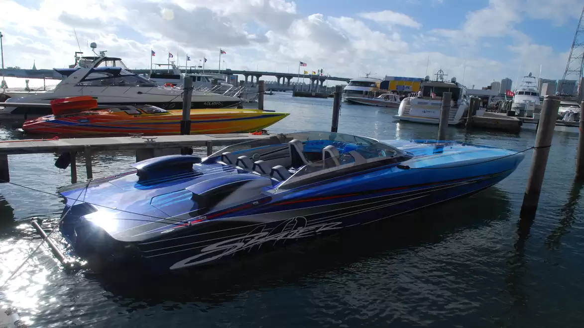 A blue speedboat anchored in a harbor, surrounded by other boats on a clear day.