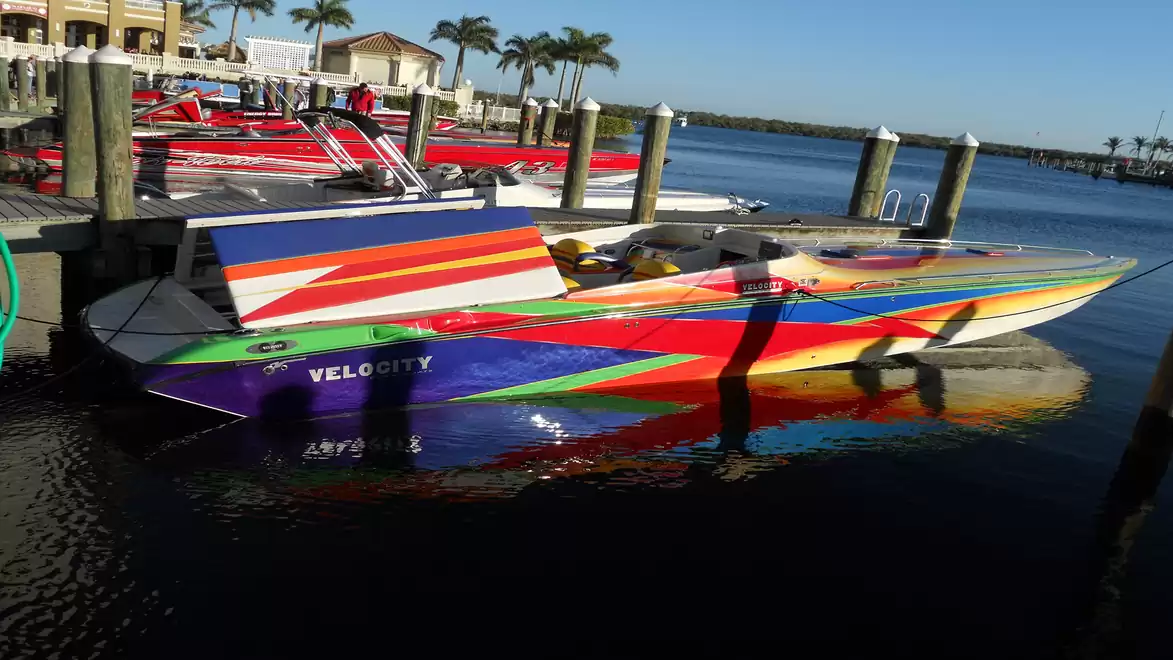 A colorful racing boat named Velocity at a dock, surrounded by palm trees and multiple berths.