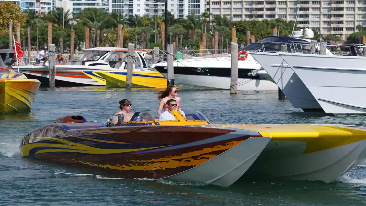 People riding a colorful speedboat in a harbor, with other boats in the background.