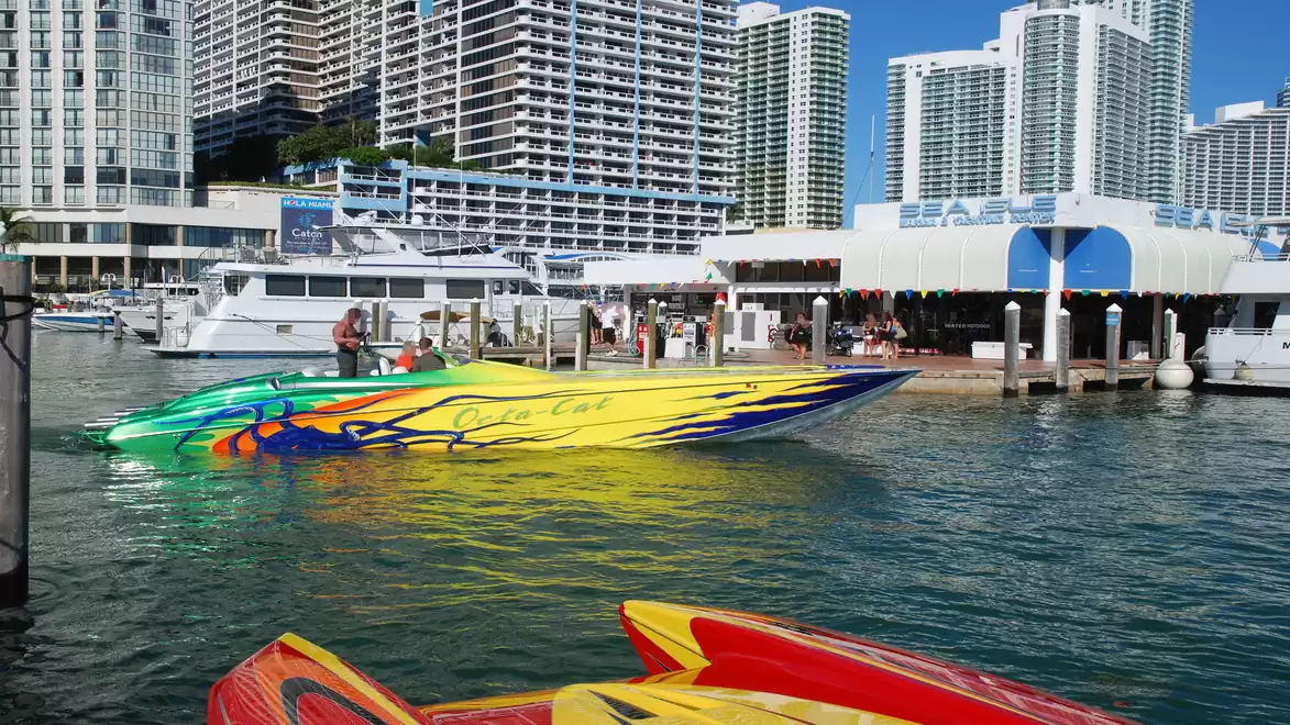 Colorful speedboat on a river in front of modern skyscrapers and a harbor scene.