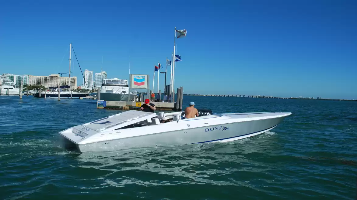 A fast motorboat navigates through a harbor under clear skies with modern buildings and bridges in the background.