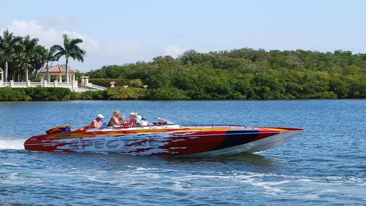 A fast motorboat with several people gliding over a calm river, surrounded by lush greenery and palm trees.