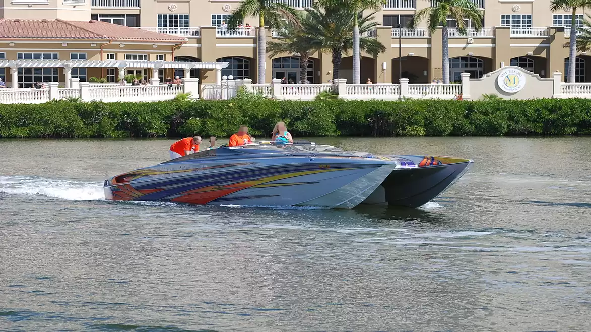Fast motorboat cruising on a river in front of a building with palm trees.