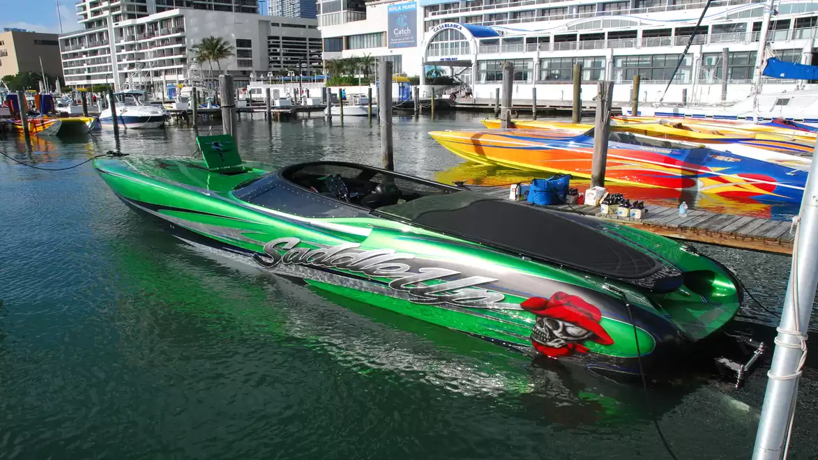 Green speedboat in the harbor, with lettering and modern buildings in the background.